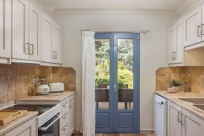 A compact kitchen with white cabinetry, a blue door, and a view of greenery outside.