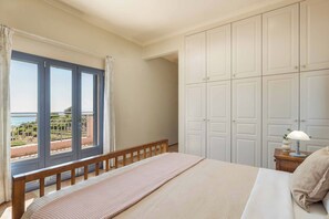 Un dormitorio con una cama grande, una mesita de noche con lámpara, un armario y un balcón con vistas al mar.