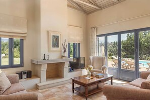Amplia sala de estar con chimenea, televisión y vistas a una piscina y jardín.