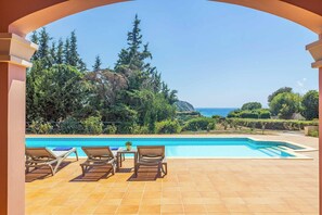 Ein Poolbereich mit Liegestühlen und Blick aufs Meer.