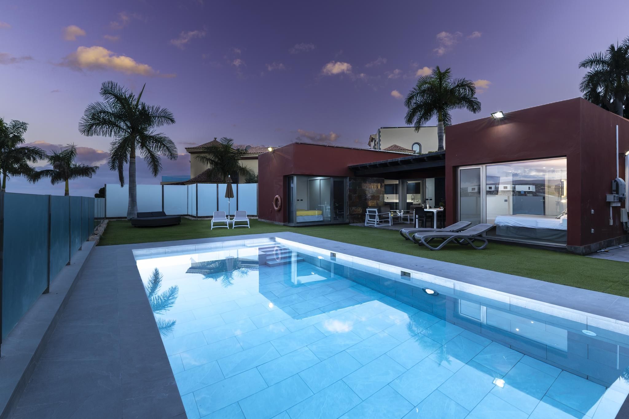 Una casa moderna con piscina, mobiliario exterior y palmeras.