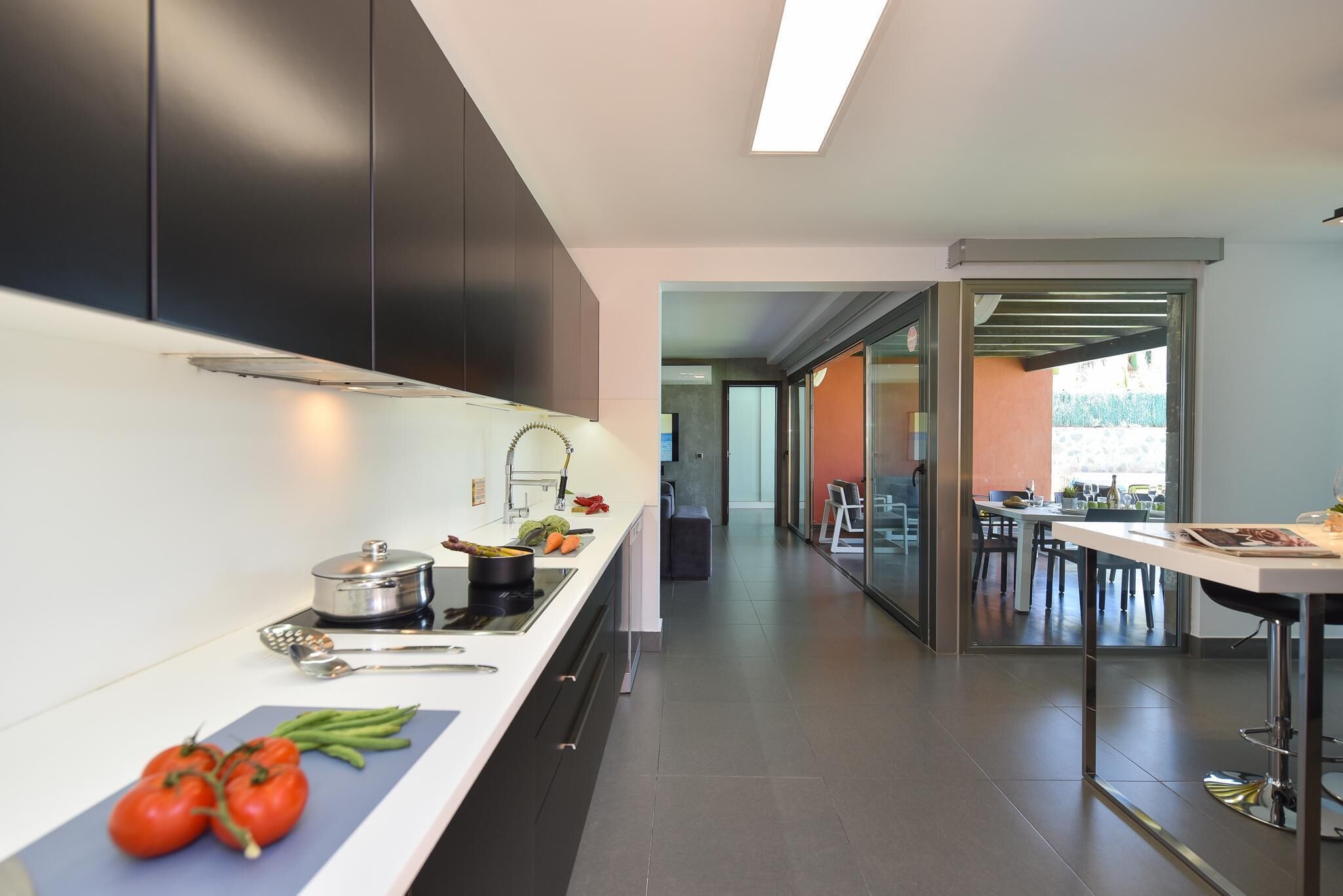 Una cocina moderna con armarios oscuros, encimera blanca y vistas a un comedor.