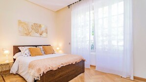 Una camera da letto con un letto in legno, biancheria da letto bianca e un'ampia finestra con tende leggere.