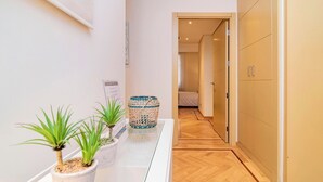 Un corridoio con piante in vaso, un tavolino di vetro e un pavimento in legno che conduce a una stanza con un letto.