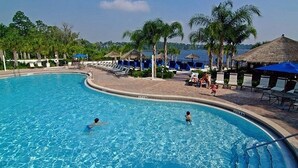 Ein Swimmingpool mit Liegestühlen und Sonnenschirmen, umgeben von Palmen und Blick auf das Meer.