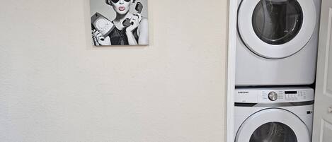 A wall-mounted Samsung washing machine with a control panel, a power outlet, and a black and white photograph of a woman with curlers and a rotary dial telephone.