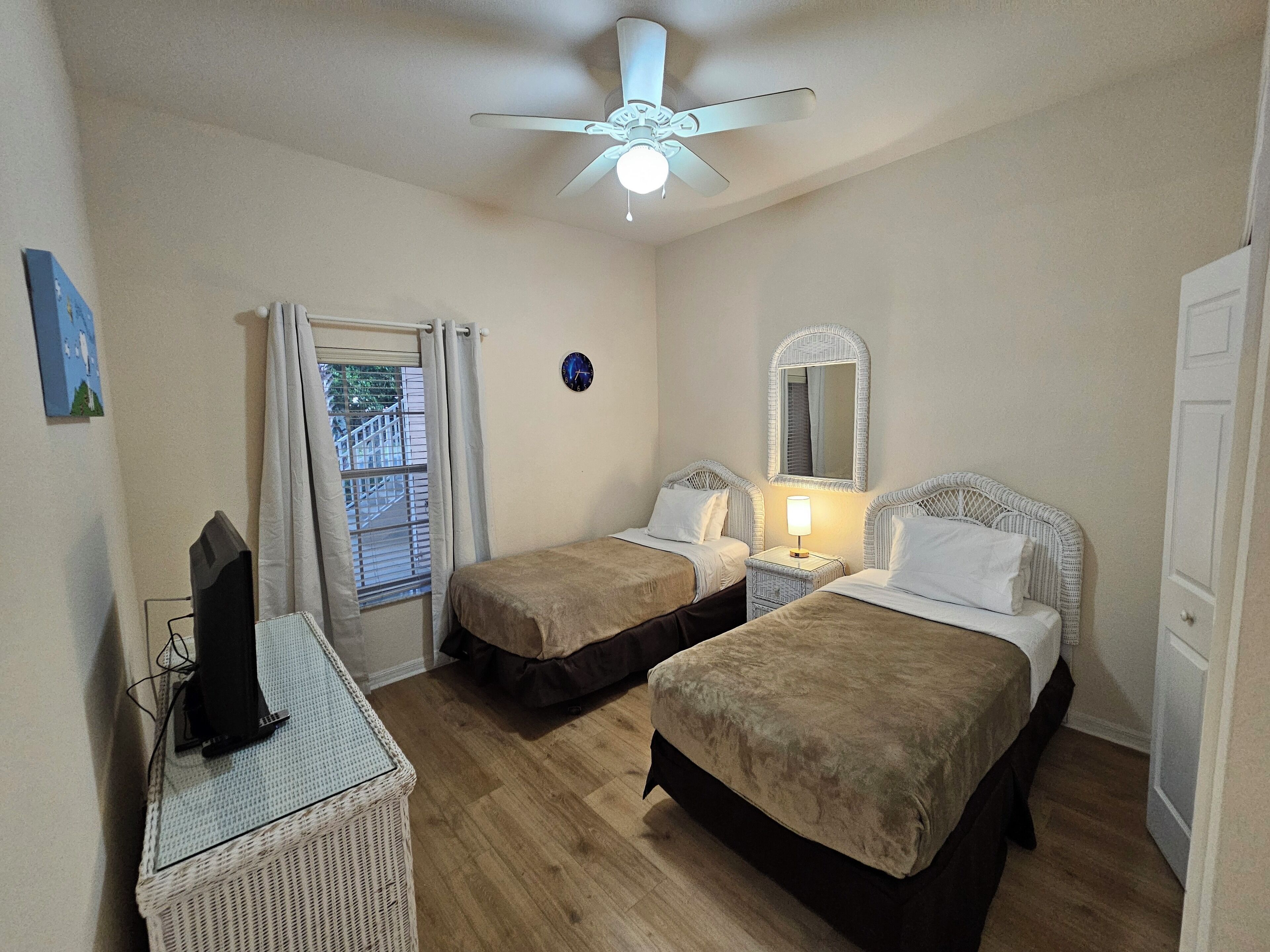 Une chambre d’hôtel avec deux lits, un ventilateur de plafond, une petite table avec une lampe et un téléviseur posé sur un meuble.