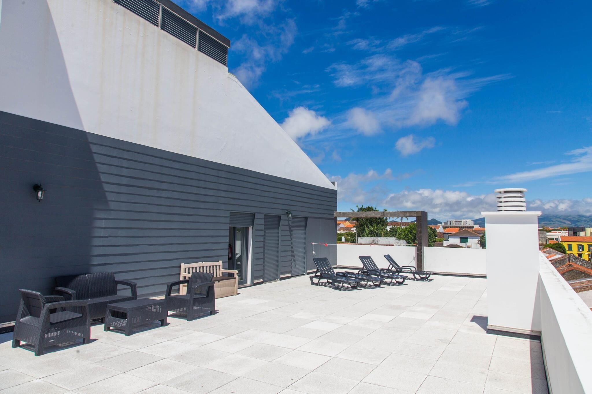A rooftop terrace with outdoor seating, a view of the city, and a modern building structure.
