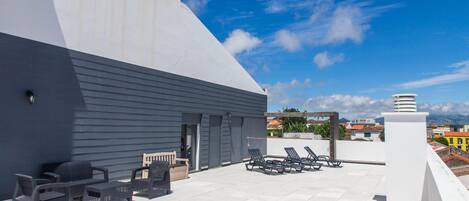 A rooftop terrace with outdoor seating, a view of the city, and a modern building structure.