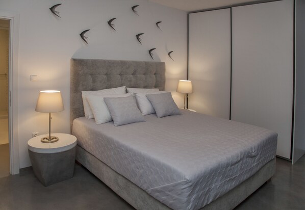A modern bedroom with a large bed, two bedside lamps, a tufted headboard, and wall-mounted bird decorations.