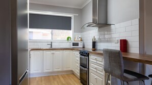 A modern kitchen with white cabinets, a microwave, a stove, and a chair. - Mrs Brightside - Tucked away in a quiet side street, Mrs. Brightside's location is sure to impress. (BRIGHT)