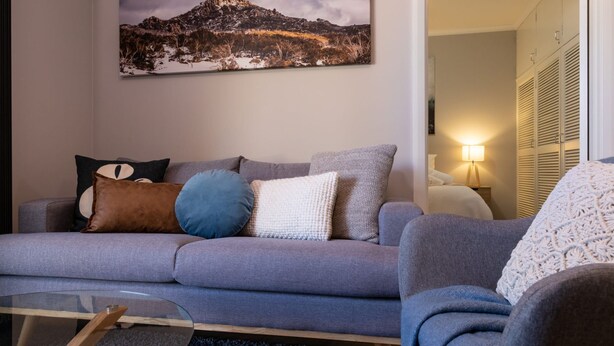 A living room with a grey sofa, multiple cushions, a glass coffee table, and a painting on the wall. - Mrs Brightside - Tucked away in a quiet side street, Mrs. Brightside's location is sure to impress. (BRIGHT)