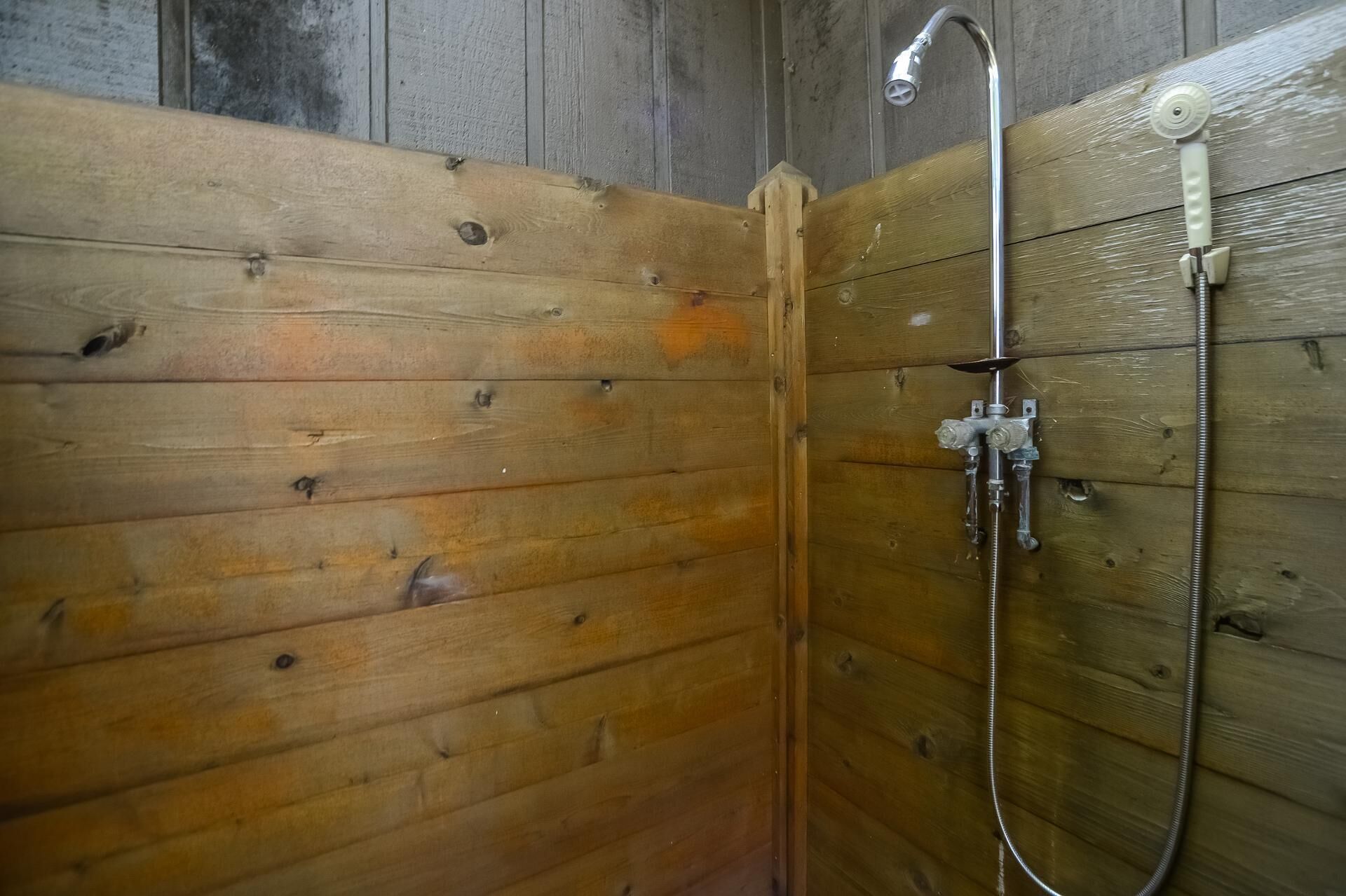 A wooden shower stall with a handheld showerhead and a hose.