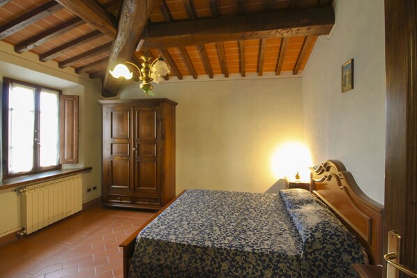 A bedroom with a wooden bed, a radiator, a window with shutters, and a wooden ceiling.