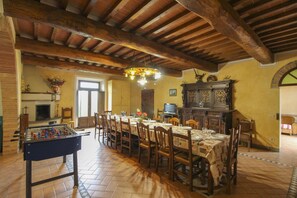 A dining area with a long table, chairs, a foosball table, a fireplace, and a television.