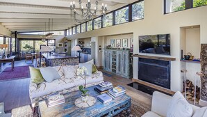 A spacious living area with a large sofa, a coffee table with books, a fireplace, and a kitchen in the background. - TABLE MOUNTAIN VILLA (Newlands)
