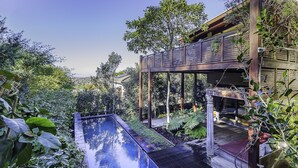 A modern outdoor pool area with a wooden deck, surrounded by lush greenery and a wooden pergola. - TABLE MOUNTAIN VILLA (Newlands)