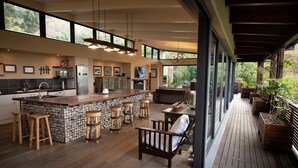 A spacious kitchen with a large island, bar stools, and a wooden deck leading to an outdoor seating area. - TABLE MOUNTAIN VILLA (Newlands)