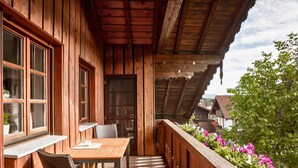 Een houten balkon met een tafel en stoelen, met uitzicht op een tuin met roze bloemen.