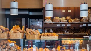 Een bakkerijdisplay met verschillende broden en gebak, prijskaartjes en hangende lampen.