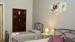 Une chambre avec deux lits, une table de chevet avec une lampe, une bibliothèque et un mur décoré de tableaux.