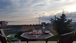 A wooden deck with a table set for two, overlooking a body of water and a distant landscape. - A House Between Mountains and Coast in a Beautiful and Quiet sea Village (Skagaströnd)