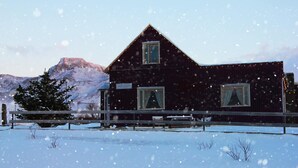 A wooden house with a sign indicating it is a guesthouse, surrounded by snow and a mountain in the background. - A House Between Mountains and Coast in a Beautiful and Quiet sea Village (Skagaströnd)