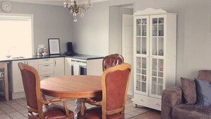A dining area with a wooden table and chairs, a kitchen with a dishwasher, and a cabinet with glass doors. - A House Between Mountains and Coast in a Beautiful and Quiet sea Village (Skagaströnd)