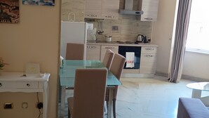 A modern kitchen with marble countertops, a dining area with a glass table and wicker chairs, and a view of the cityscape through the window. - Sistina House near Spanish Steps (Roma)