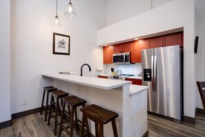 Cozinha moderna com ilha central, eletrodomésticos de aço inoxidável e banquetas de madeira.
