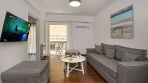 A modern living room with a grey sofa, a white coffee table, and a grey ottoman. A flat-screen TV is mounted on the wall, and there is a painting above the sofa.