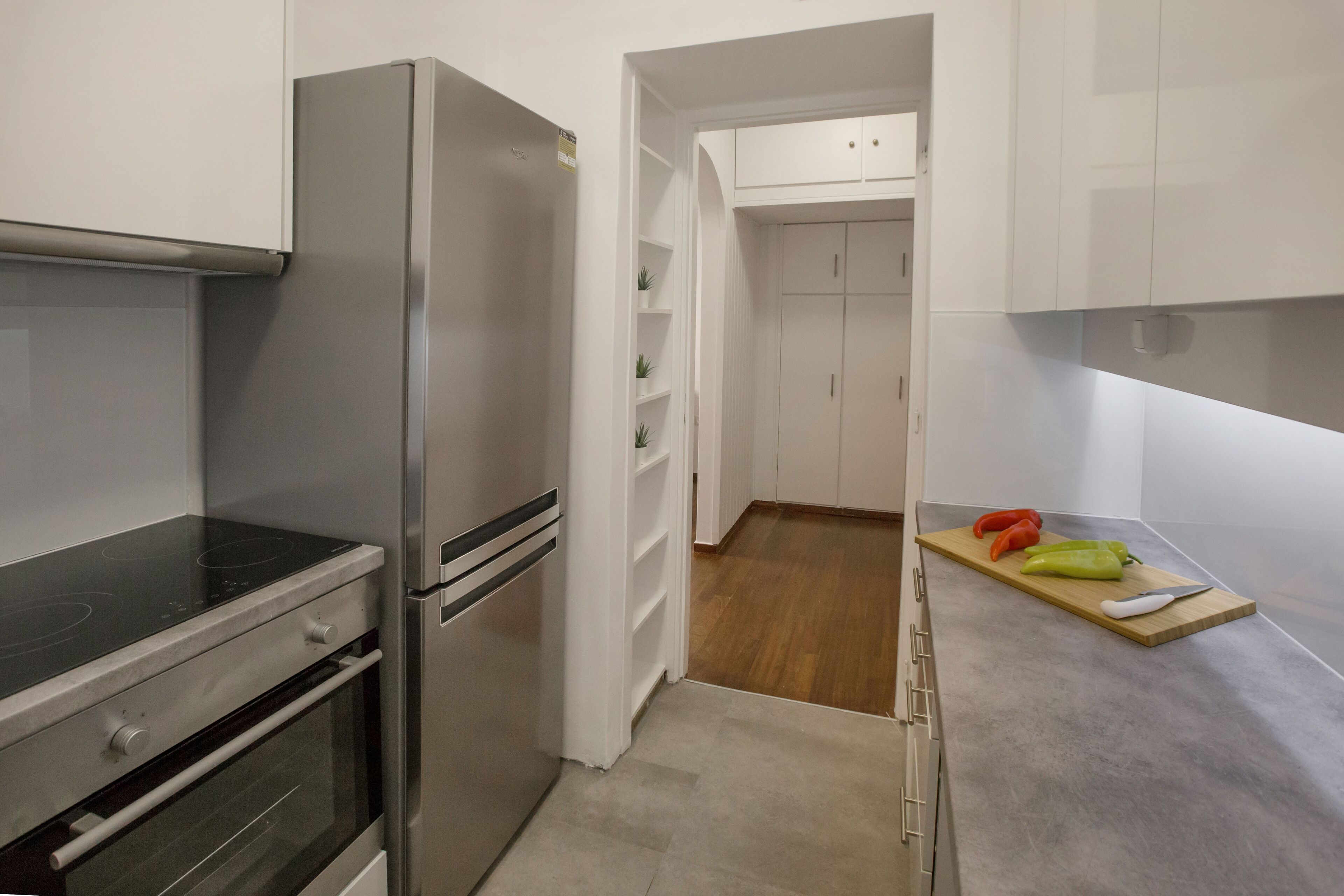 A modern kitchen with stainless steel appliances, wooden flooring, and a wooden countertop with vegetables.