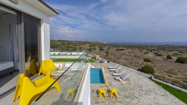 Un espace piscine extérieur moderne, avec des chaises jaunes, une balustrade en verre et une vue sur le paysage.
