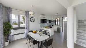 Une cuisine moderne dotée d’un îlot central, d’un coin repas avec une table blanche et des chaises noires, et d’une grande fenêtre agrémentée de rideaux.