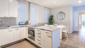 Eine moderne Küche mit weißen Schränken, einem eingebauten Ofen und einem Essbereich mit weißem Tisch und Stühlen.