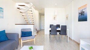A modern living room with a staircase, a dining area with chairs, and a white coffee table with a plant. - Arco Iris on the sea with pool (Callao Salvaje)