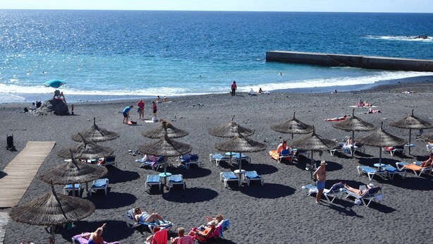 A beach with thatched umbrellas and lounge chairs, a wooden walkway, and the ocean in the background. - Arco Iris on the sea with pool (Callao Salvaje)