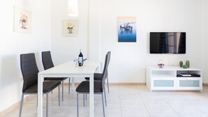 A modern dining area with a white table and four black chairs, a white cabinet with decorative items, and a flat-screen TV on the wall. - Arco Iris on the sea with pool (Callao Salvaje)