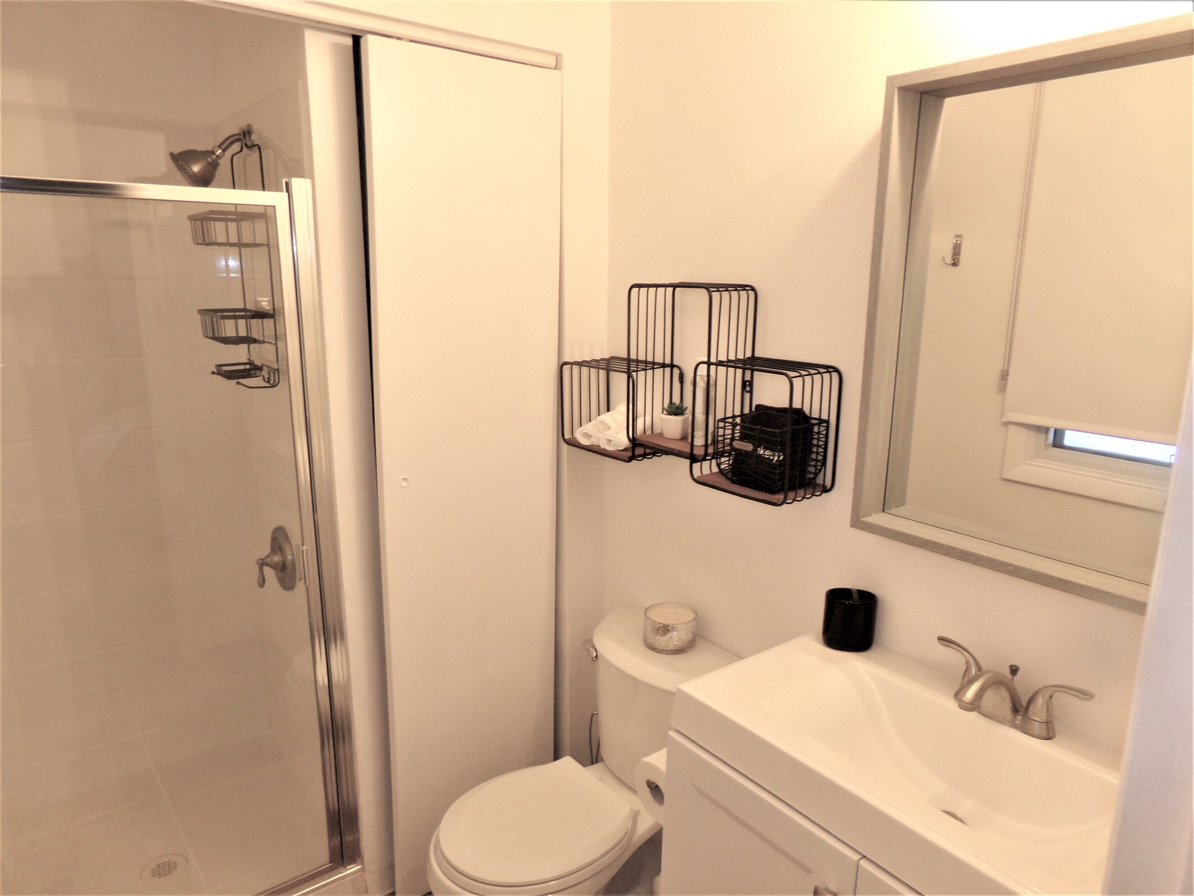 Een badkamer met een douchecabine van glas, toilet, wastafel met spiegel en twee zwarte metalen manden aan de muur.