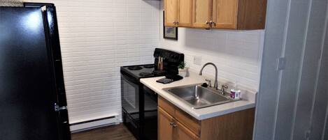 Una cocina compacta con muebles de madera, un refrigerador negro, una estufa y un lavamanos.