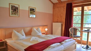 A bedroom with a wooden bed, a nightstand, a chair, and a window with a view of trees. - Vacation apartment Birnbaum 68 sqm, 2 separate bedrooms, kitchen (Neubeuern)