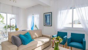 Uma sala de estar moderna com um sofá bege, poltronas verde-água e uma mesa de centro com um vaso de flores.