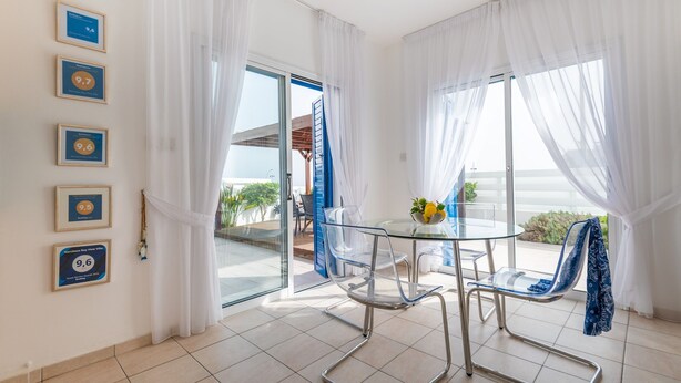 Uma sala de jantar moderna com mesa e cadeiras de vidro, cortinas brancas e prêmios emoldurados na parede.
