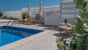 Área de piscina no terraço com piscina azul cristalina, cadeiras de descanso, guarda-sóis e um aviso com as regras da piscina.