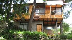 A wooden cabin with a balcony, surrounded by trees and vegetation.