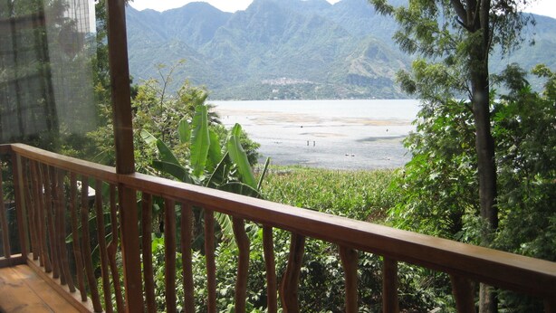 A balcony with a wooden railing overlooking a lake and mountains.