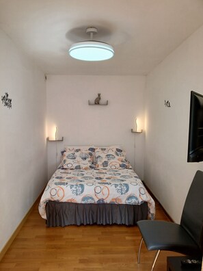 A bedroom with a bed, a chair, a ceiling light, and wall-mounted sconces.