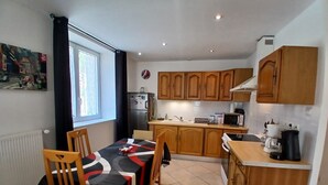 A compact kitchen with wooden cabinets, a dining table with chairs, a refrigerator, a microwave, and a coffee maker. - Comfortable 2bed/ 6-person apartment (Saint-Rambert-en-Bugey)