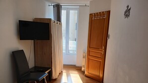 A room with a bed, a TV mounted on the wall, a chair, a wooden door, and a window with curtains. - Comfortable 2bed/ 6-person apartment (Saint-Rambert-en-Bugey)