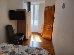 A room with a bed, a TV mounted on the wall, a chair, a wooden door, and a window with curtains. - Comfortable 2bed/ 6-person apartment (Saint-Rambert-en-Bugey)